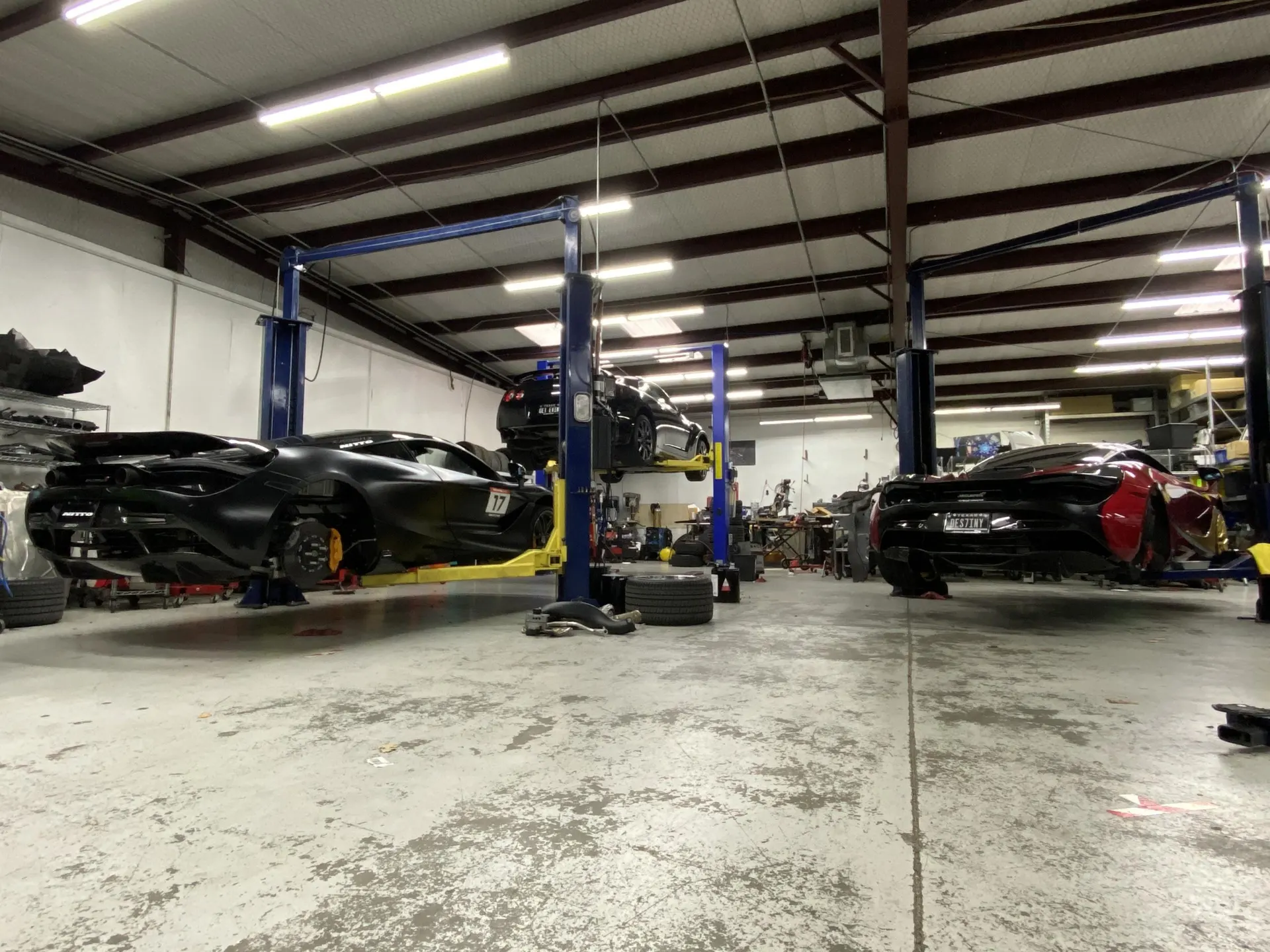 Multiple McLaren supercars on lifts in a performance tuning shop garage, undergoing maintenance or modifications.
