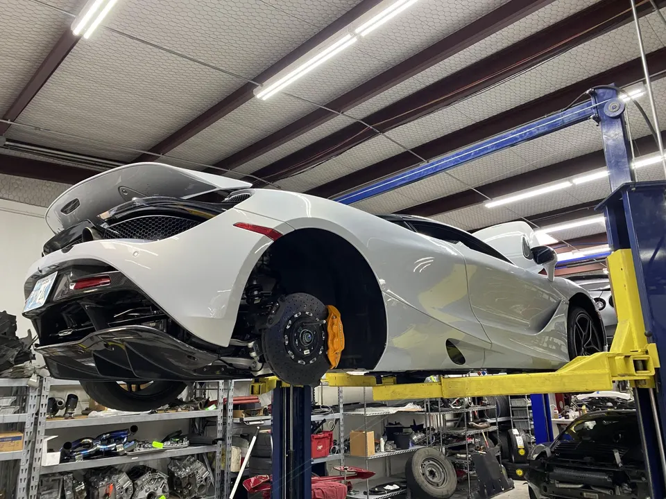 White McLaren 720S on a car lift in a performance tuning shop, with its rear wheels removed exposing the brakes.