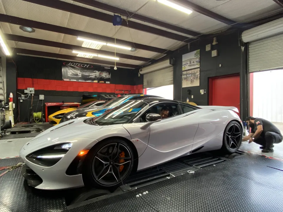 A silver McLaren 720S on a dyno at Jotech Motorsports, with a technician working near the rear wheel.