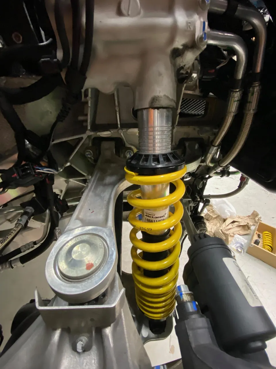 Close-up of a McLaren suspension system featuring a yellow coil spring and shock absorber during installation.