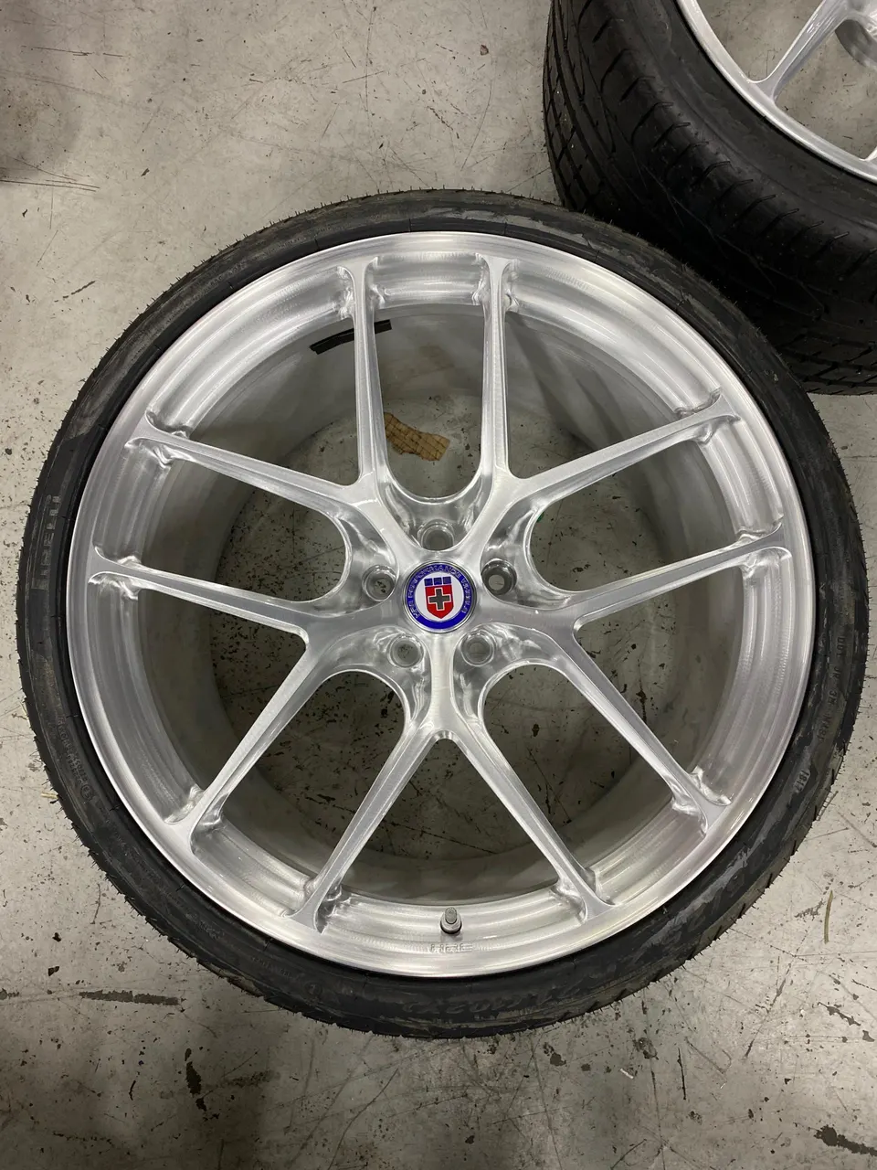 Close-up of a silver HRE performance wheel with a tire on a shop floor.