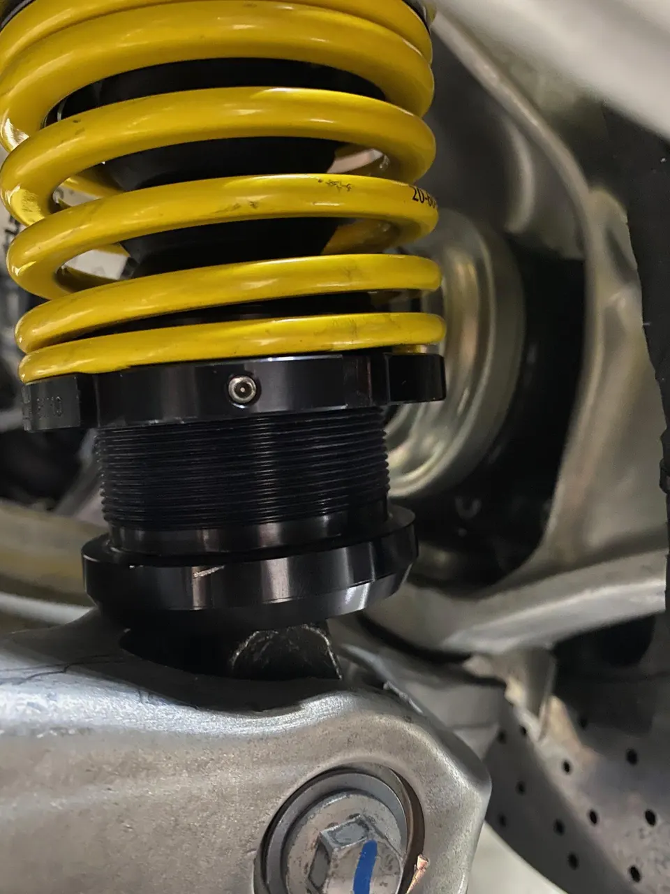 Close-up of a yellow coilover suspension system installed on a performance car chassis, highlighting the spring and adjustment collar.