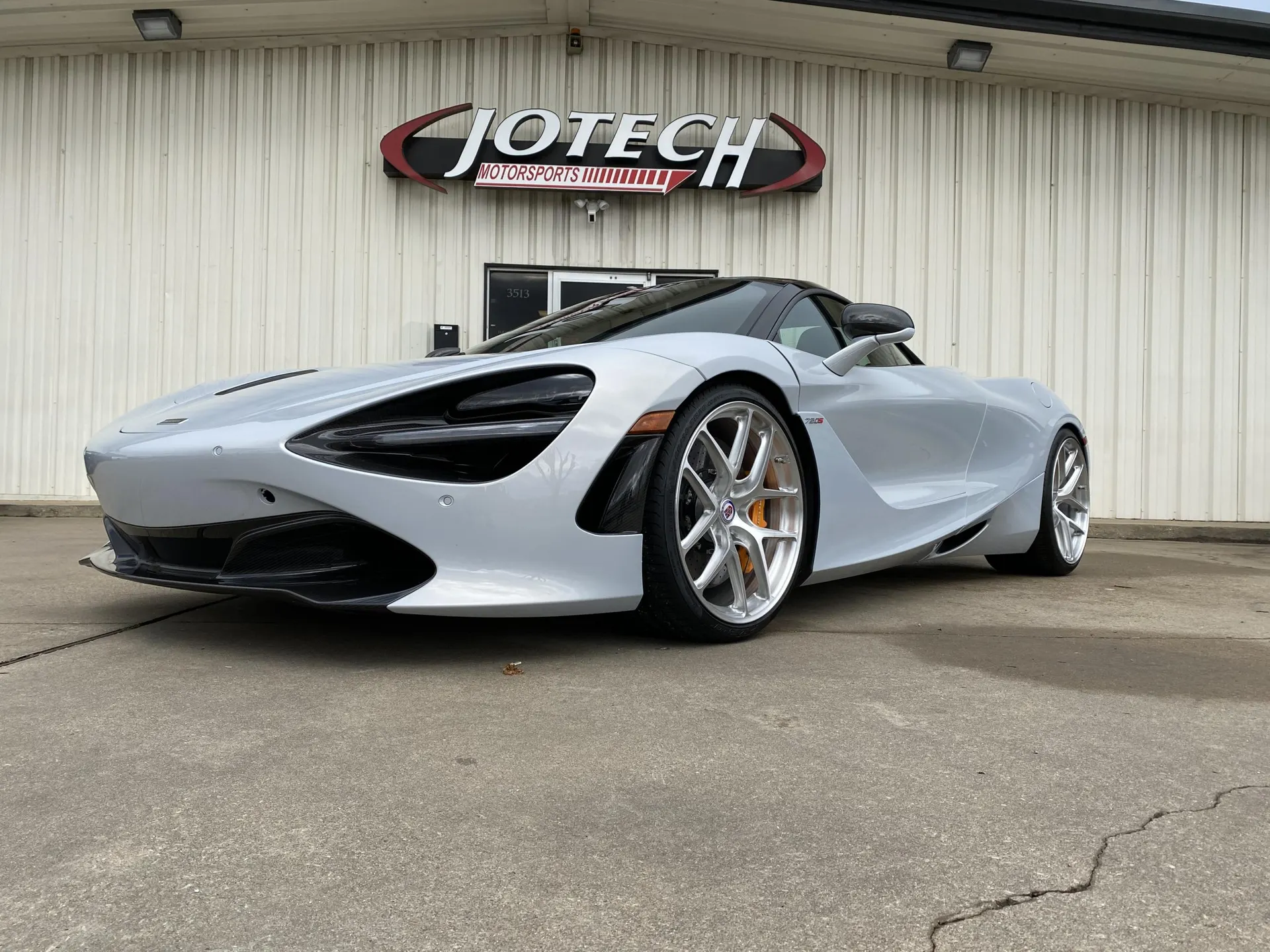 A silver McLaren 720S supercar with aftermarket wheels parked in front of the Jotech Motorsports shop.