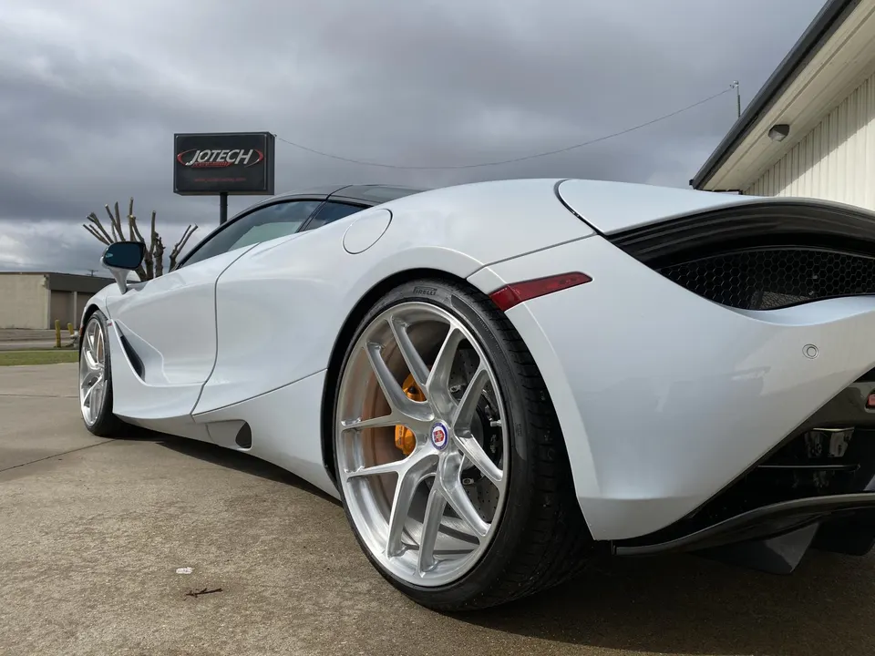 A white McLaren 720S with aftermarket silver wheels and orange brake calipers parked outside Jotech Motorsports.