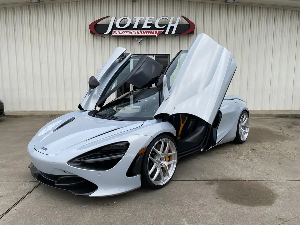 Silver McLaren 720S supercar with butterfly doors open, parked outside Jotech Motorsports performance tuning shop.