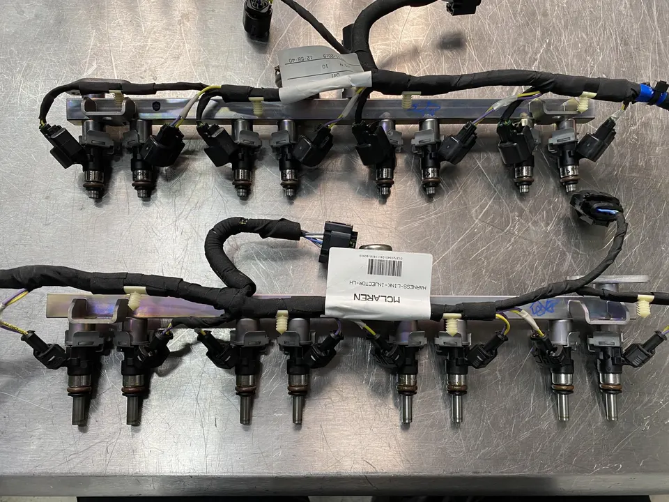 McLaren fuel injectors and fuel rails laid out on a workbench in a performance tuning shop.