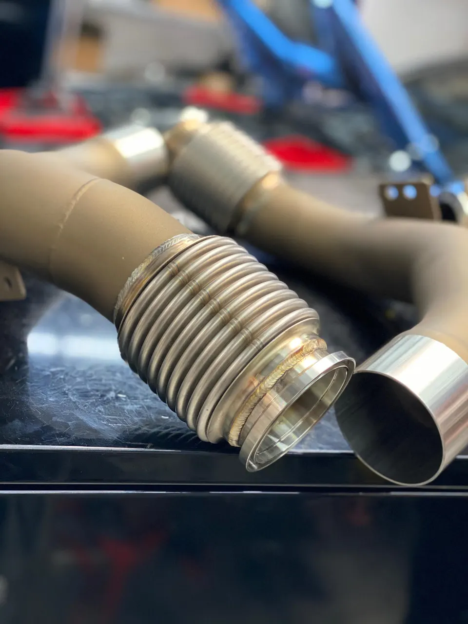 Close-up of custom fabricated exhaust piping with visible welds on a workbench in a performance shop.