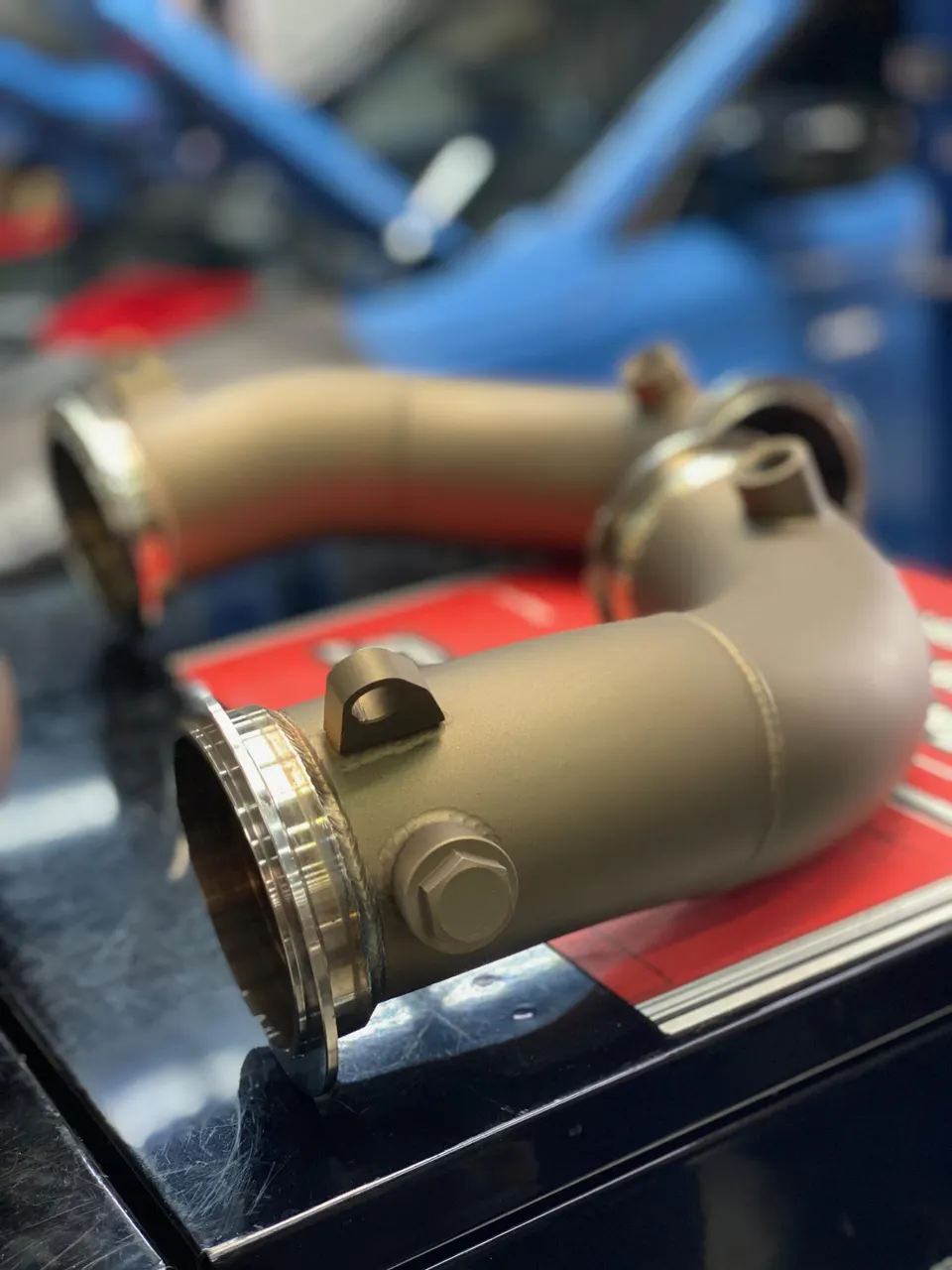 Titanium downpipes for a performance vehicle on a workbench in a tuning shop.