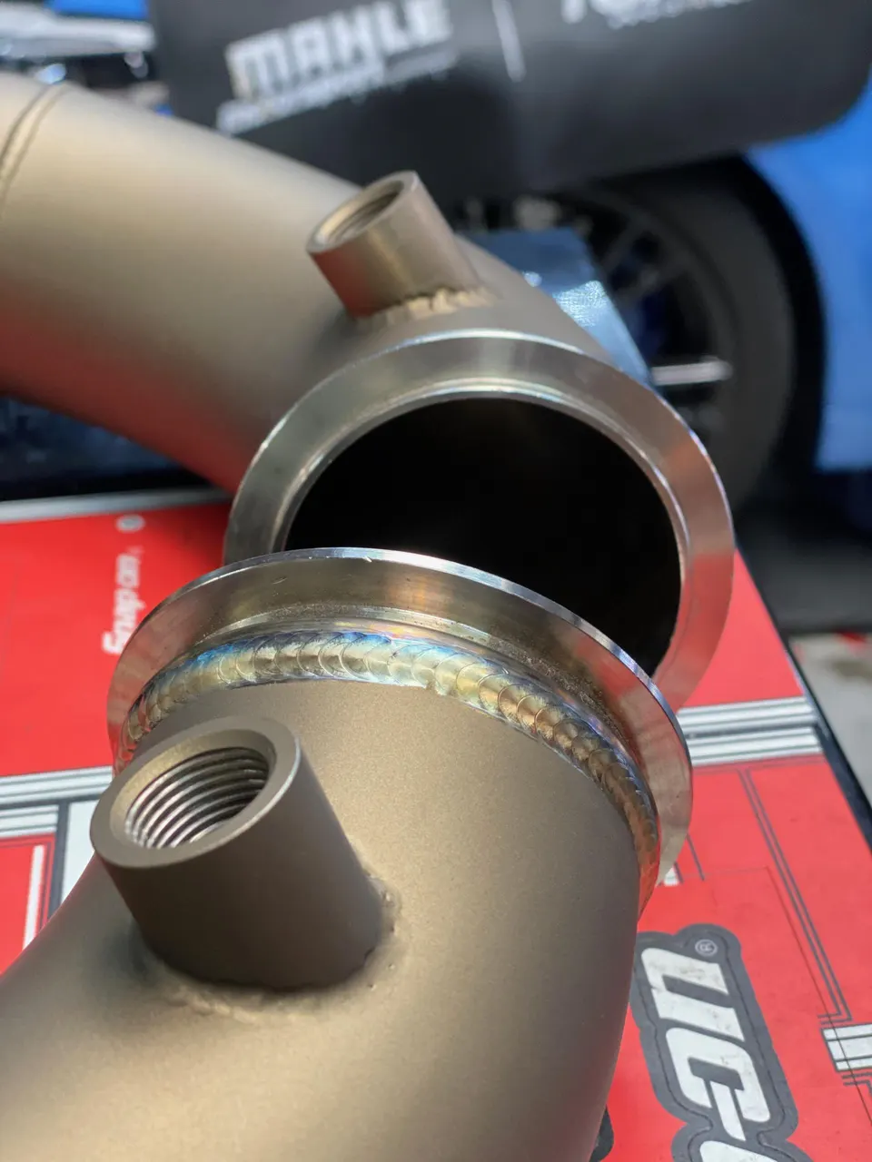 Close-up of custom titanium exhaust pipes with visible welds, likely downpipes, in a performance tuning shop.