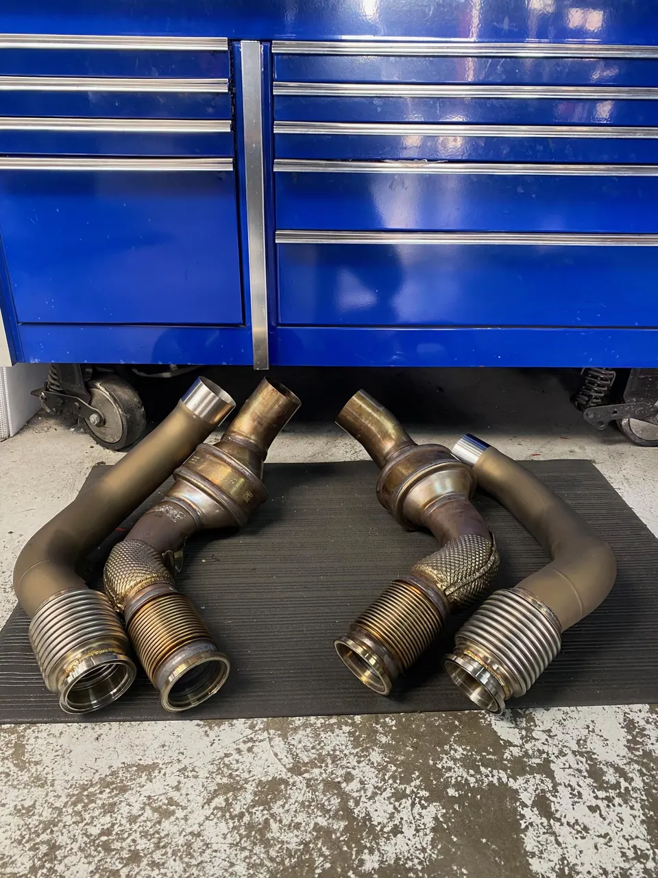 Aftermarket exhaust downpipes for a performance car laid out in a shop, ready for installation.