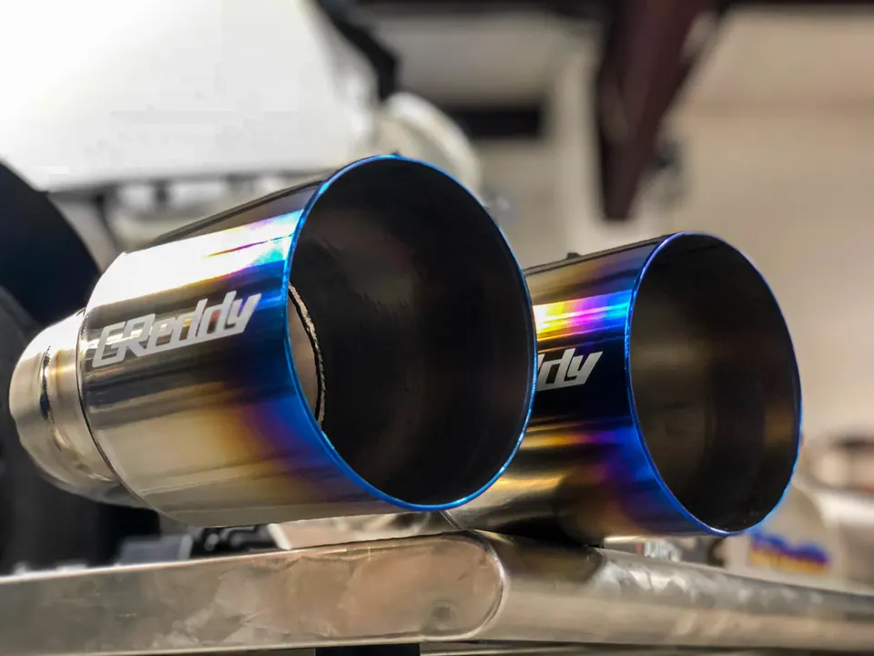 Close-up of GReddy titanium exhaust tips with a burnt finish, showcasing aftermarket performance parts.