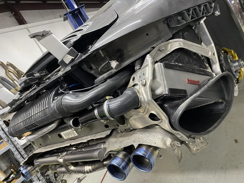 Underside view of a performance car on a lift, showcasing a Garrett intercooler, carbon fiber parts, and a custom exhaust.