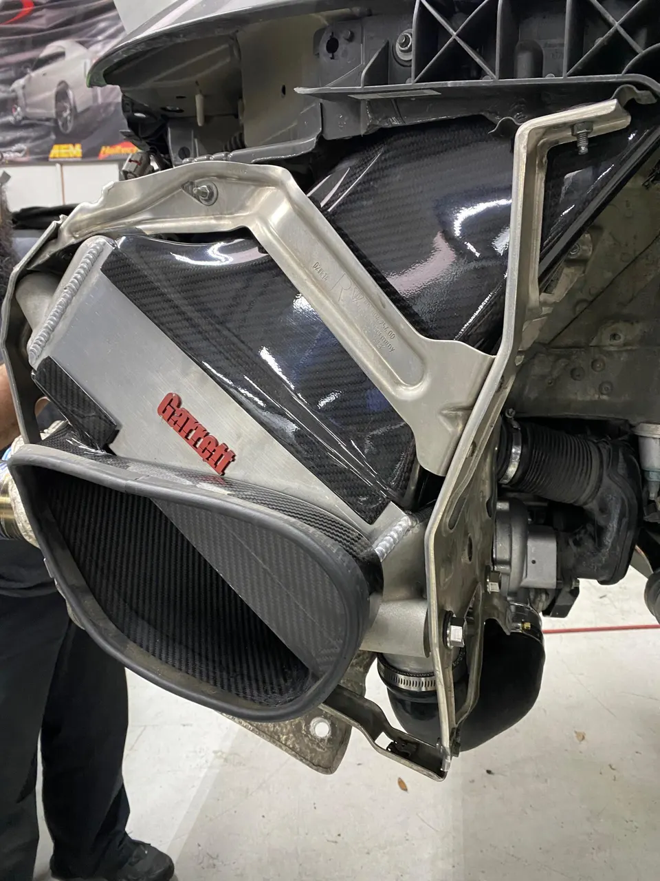 Close-up of a Garrett carbon fiber induction system being installed in a performance car at a tuning shop.
