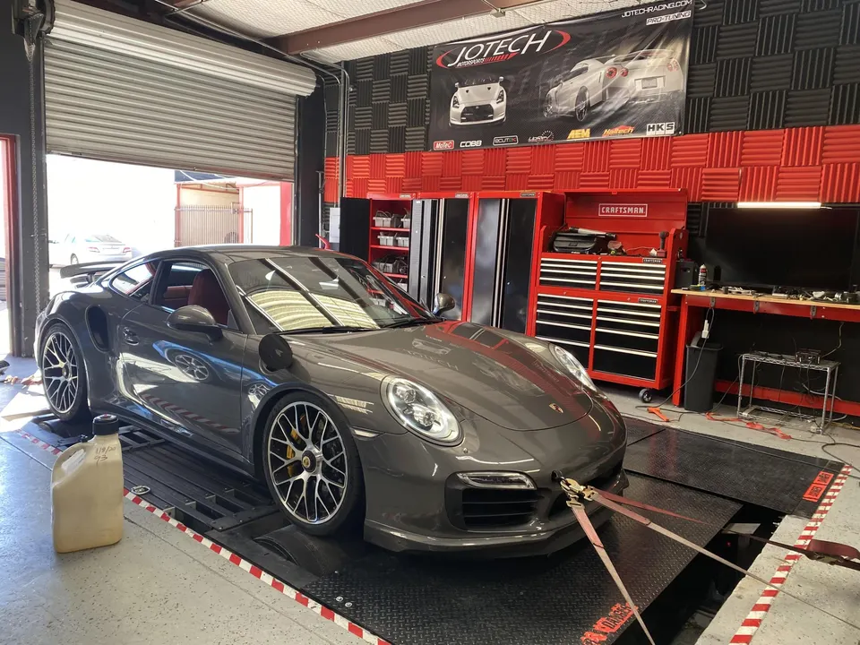 A grey Porsche 911 Turbo S strapped to a dynamometer at Jotech Motorsports for performance tuning.