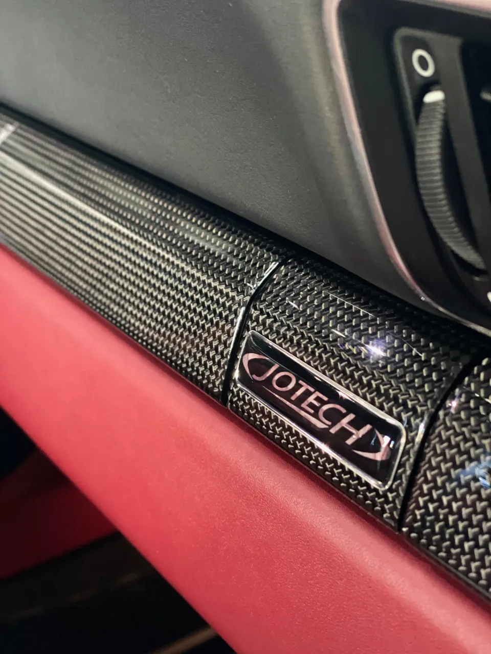 Close-up of Jotech carbon fiber interior trim with red leather accents in a high-performance car interior.