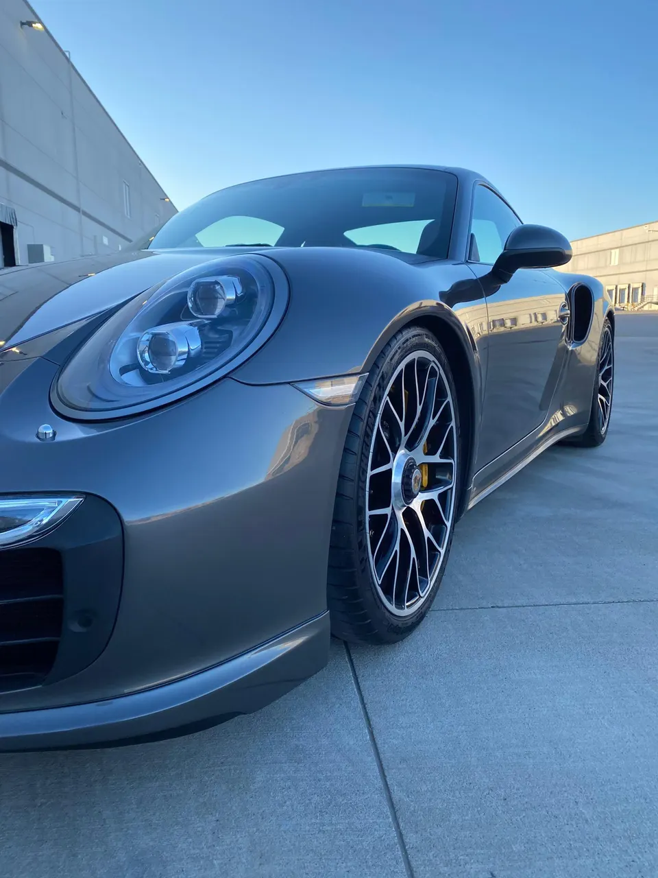 Grey Porsche 911 parked outdoors, showcasing its front design, multi-spoke wheels, and yellow brake calipers.
