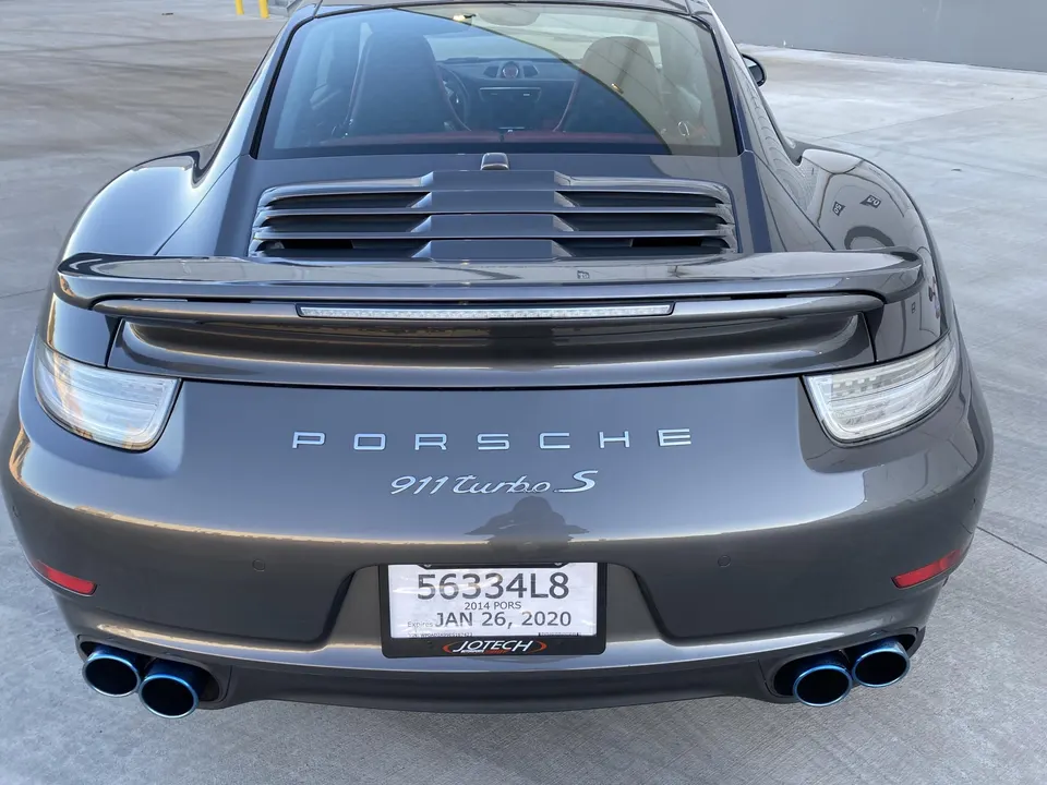 Rear view of a grey Porsche 911 Turbo S with aftermarket blue exhaust tips parked on a concrete lot.