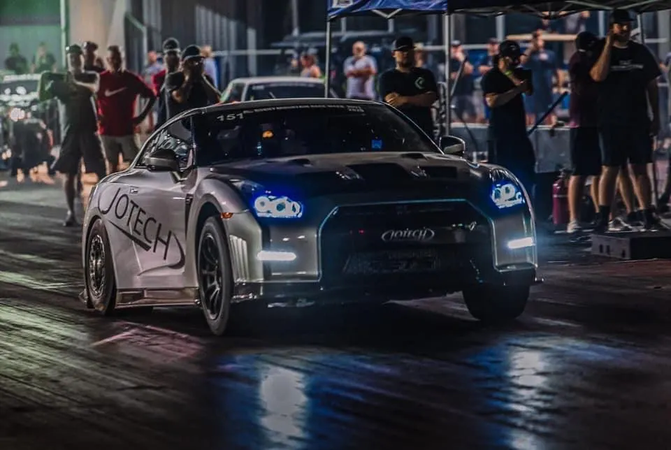Jotech Nissan GT-R on a drag strip at night, with spectators in the background.