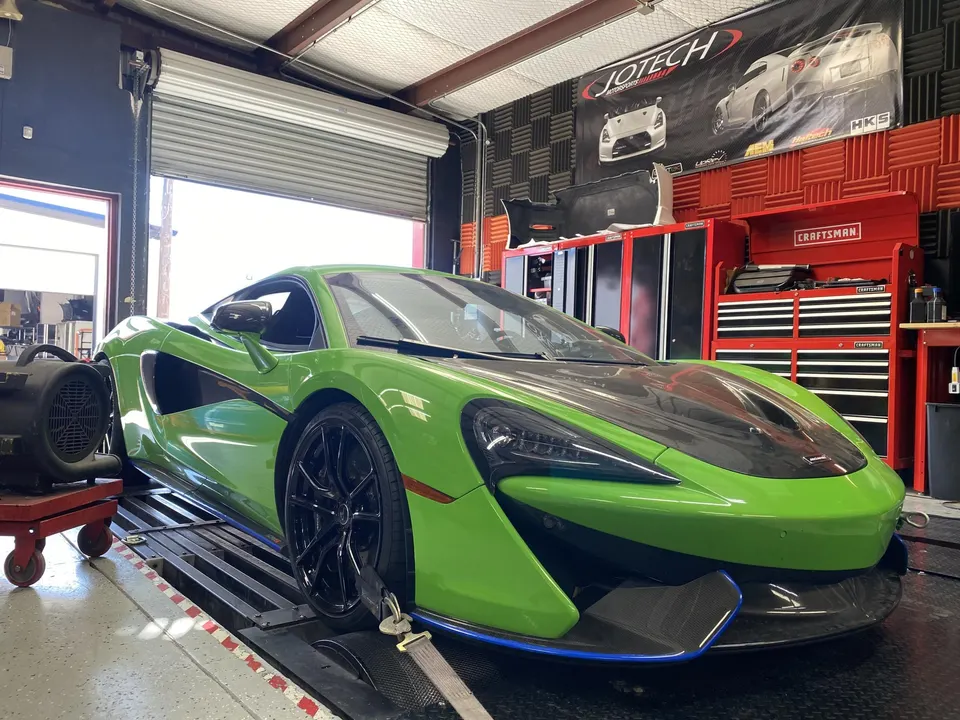 A green McLaren supercar strapped to a dyno at Jotech Motorsports performance tuning shop.