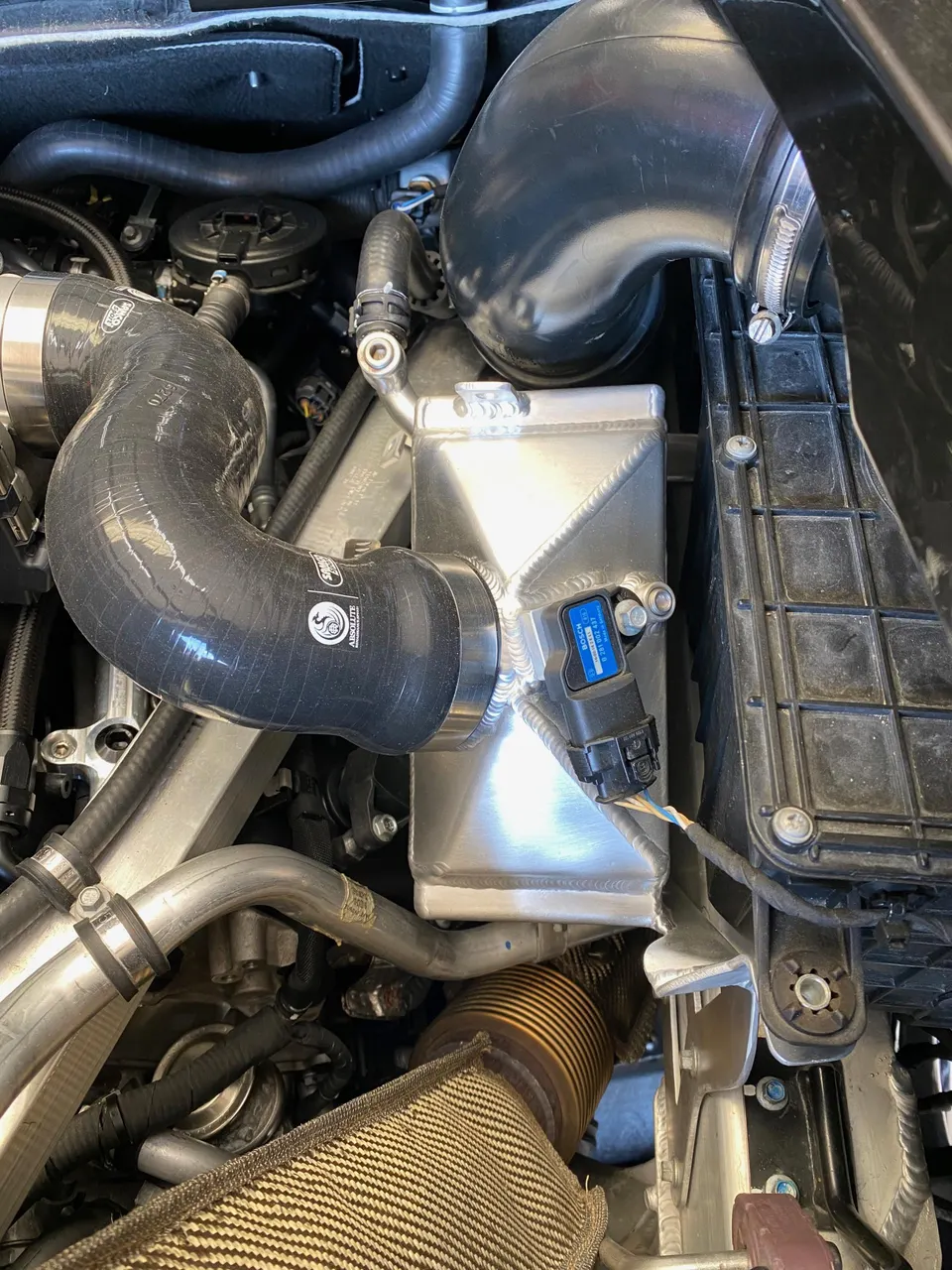 Close-up of a modified engine bay showing aftermarket intercooler, boost piping, and exhaust components.