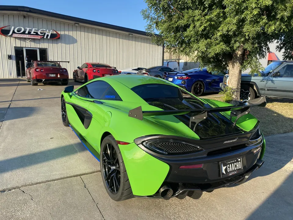 The exterior of Jotech Motorsports performance shop with a bright green McLaren, two red Nissan GT-Rs, and other supercars parked outside.