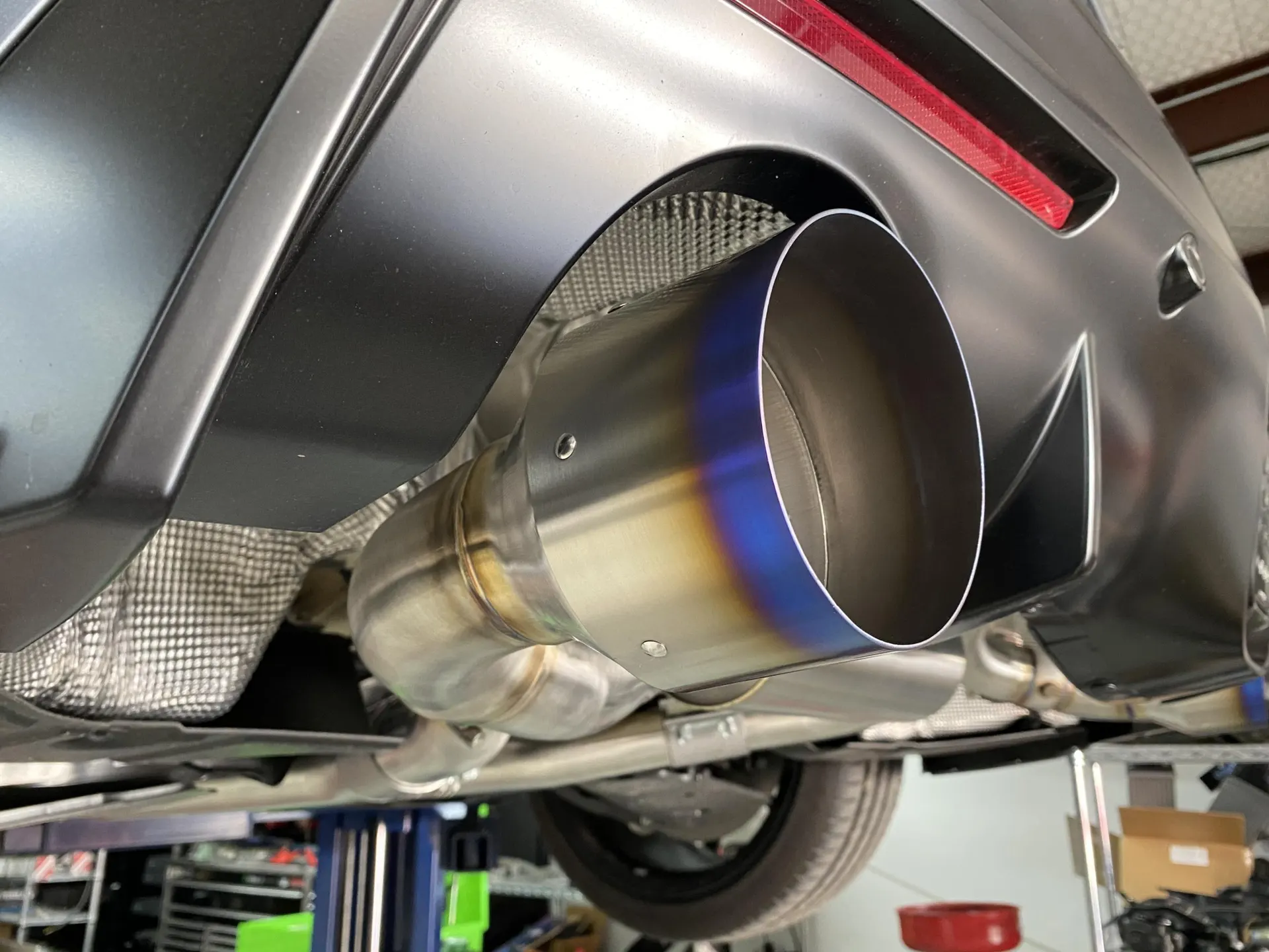 Close-up of a performance exhaust system with a burnt titanium tip installed on the underside of a car in a shop.