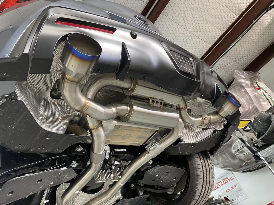 Aftermarket exhaust system with titanium tips installed on a grey Toyota Supra underbody.
