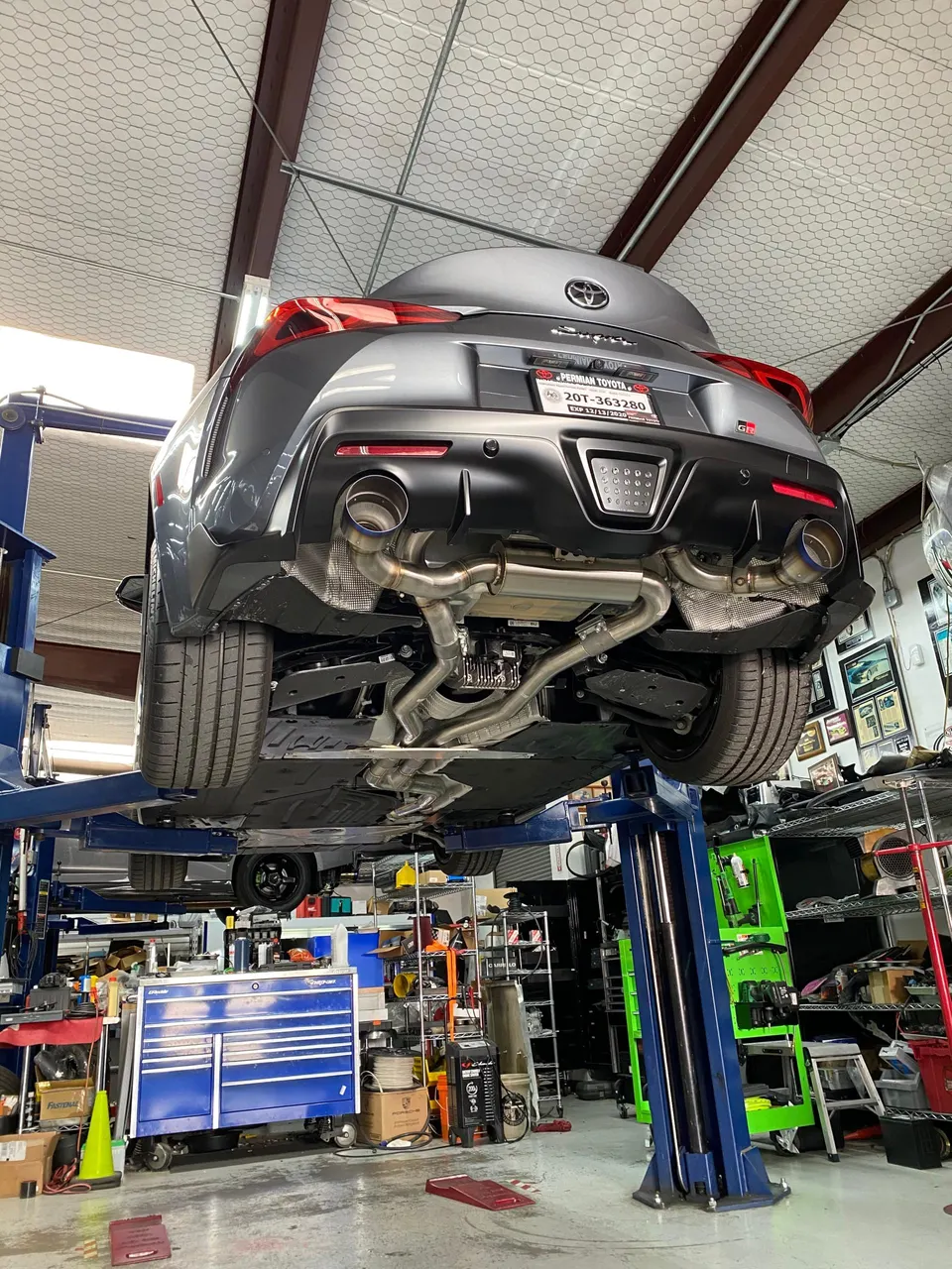 Rear view of a grey Toyota GR Supra on a lift in a shop, showcasing an aftermarket exhaust system.