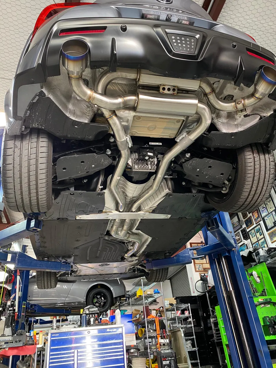 A Toyota Supra on a lift in a shop, showcasing its aftermarket exhaust system with titanium tips and underbody.