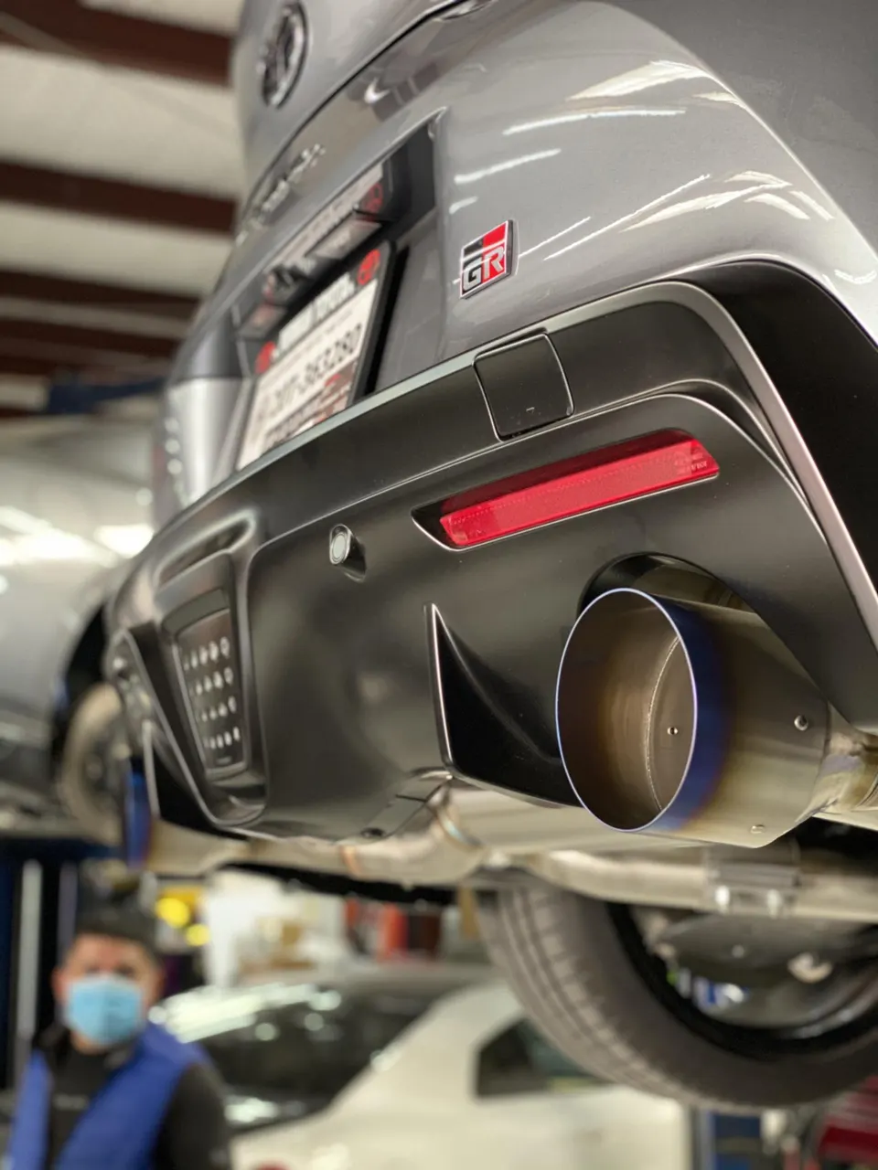 Rear view of a Toyota GR Supra on a lift in a shop, showcasing an aftermarket exhaust system.