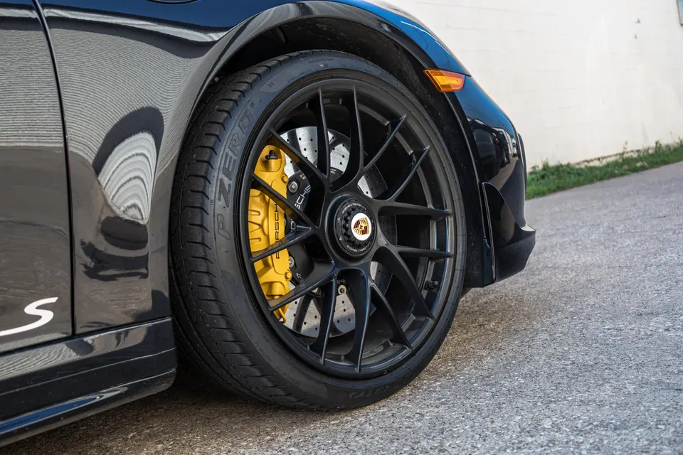 Close-up of a black Porsche's front wheel with black multi-spoke rims and yellow brake calipers.