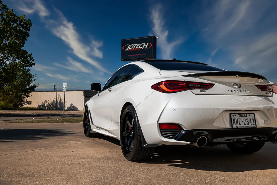 White Infiniti Q60S with aftermarket wheels, performance exhaust, and rear spoiler parked at Jotech Motorsports.