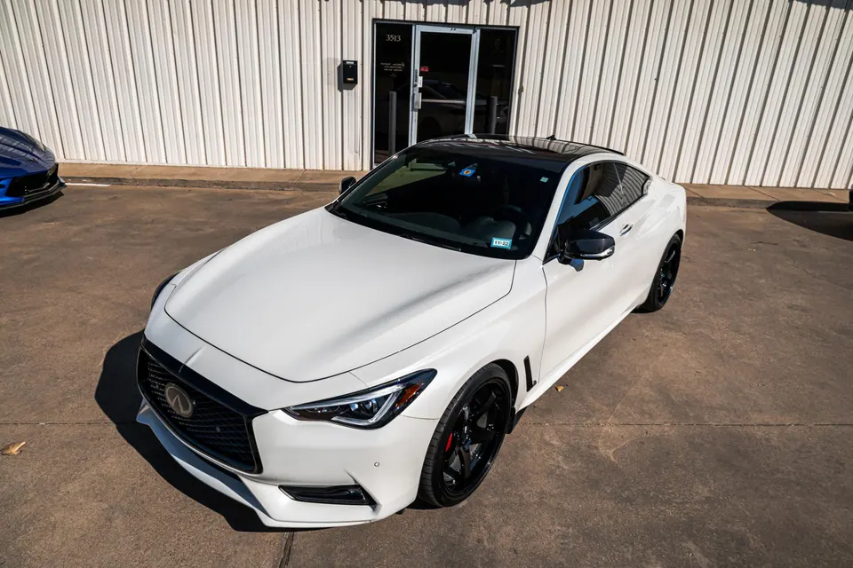 White Infiniti Q60 coupe with a black roof and black wheels parked outside a building on a sunny day.