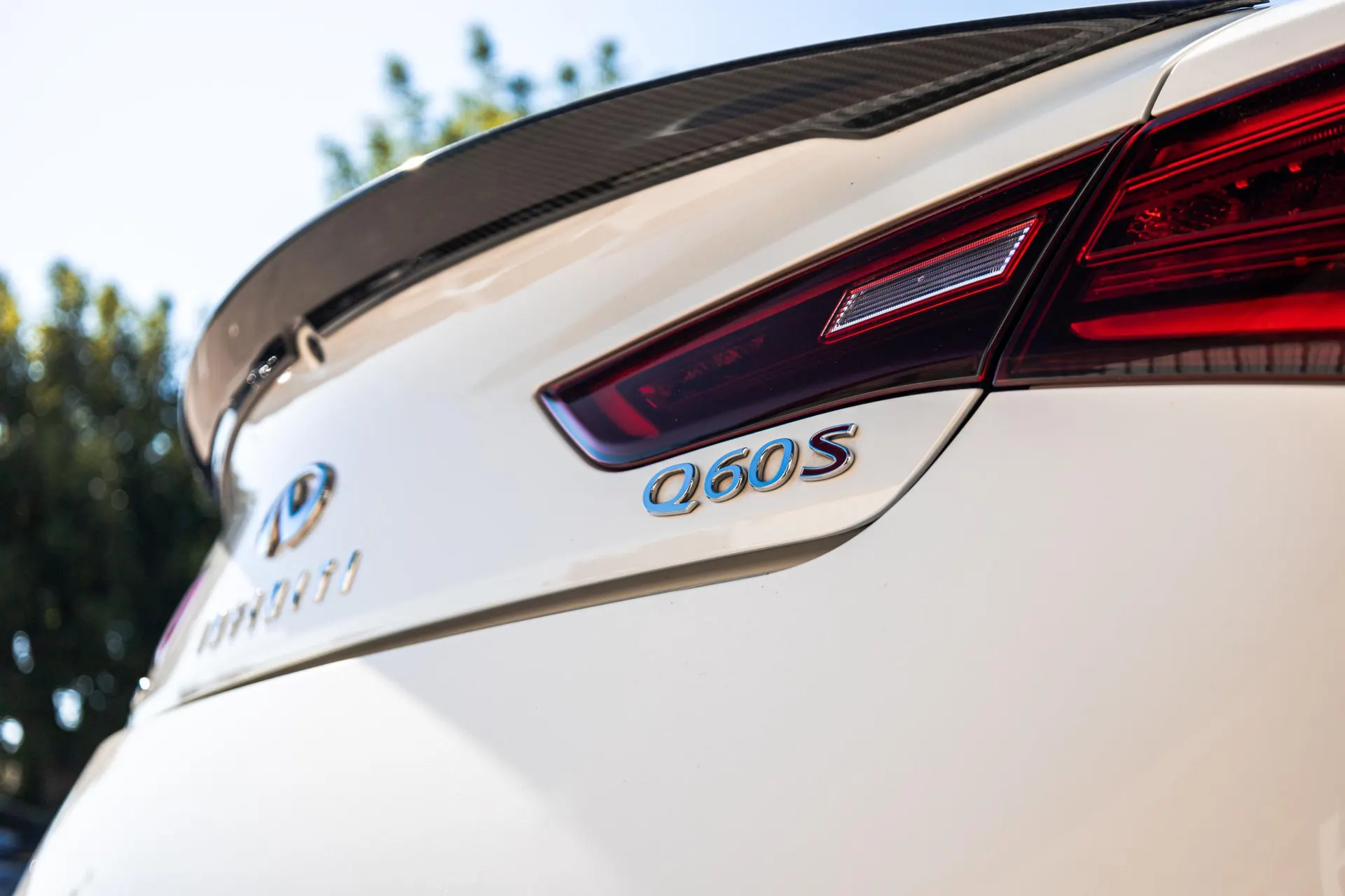 Close-up of the rear of an Infiniti Q60S with a carbon fiber spoiler and taillight.