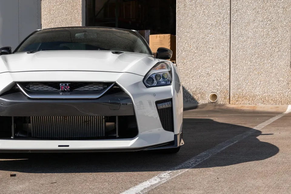 Front view of a white Nissan GT-R R35 with an aftermarket intercooler visible, parked outside a building.