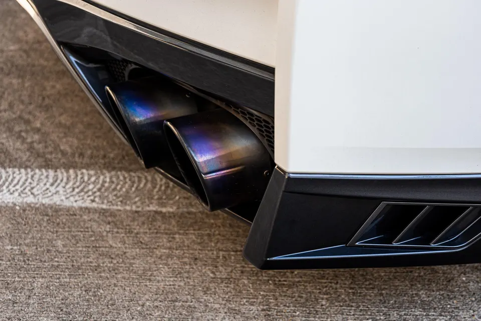 Close-up of iridescent titanium exhaust tips on a white sports car's rear bumper, showcasing the detail.