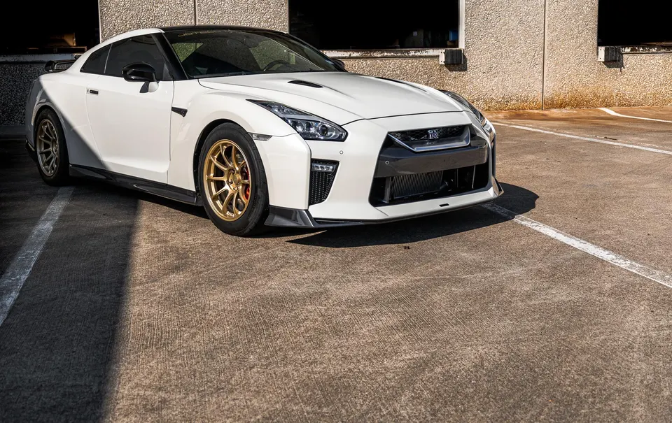 White Nissan GT-R with gold wheels parked in a lot, showcasing its sleek design and aftermarket modifications.