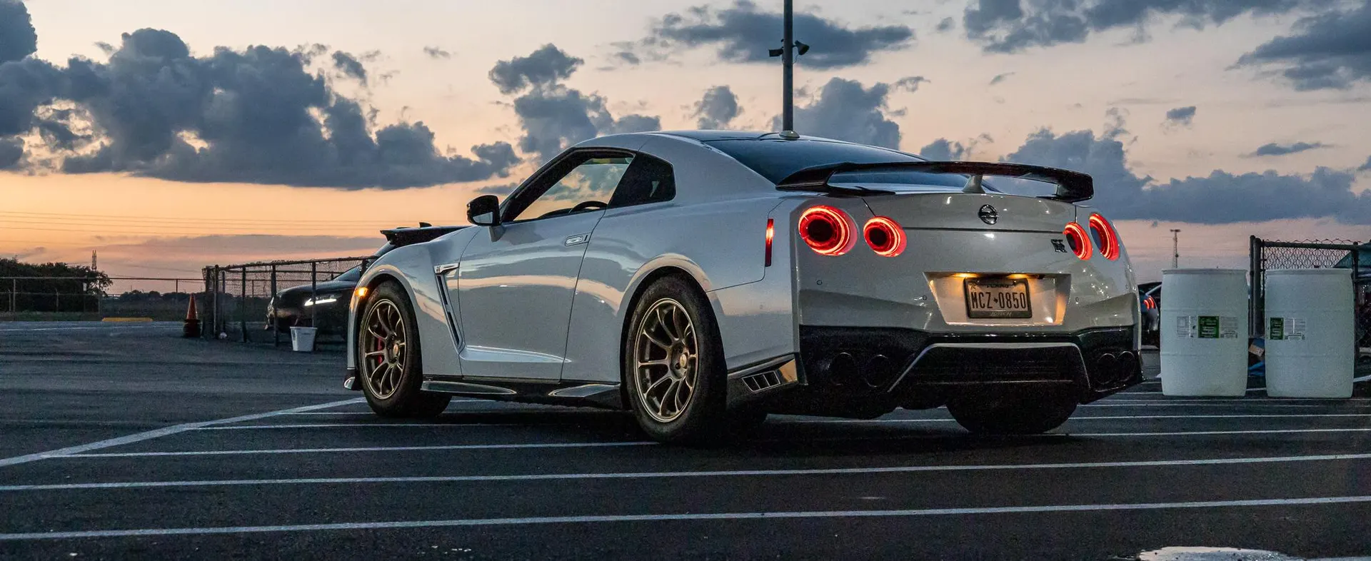 White Nissan GT-R R35 with aftermarket wheels parked at a track during sunset.