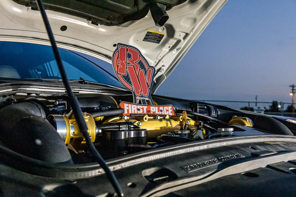 A close-up of a custom engine bay featuring a gold intake manifold and a 'First Place' trophy.