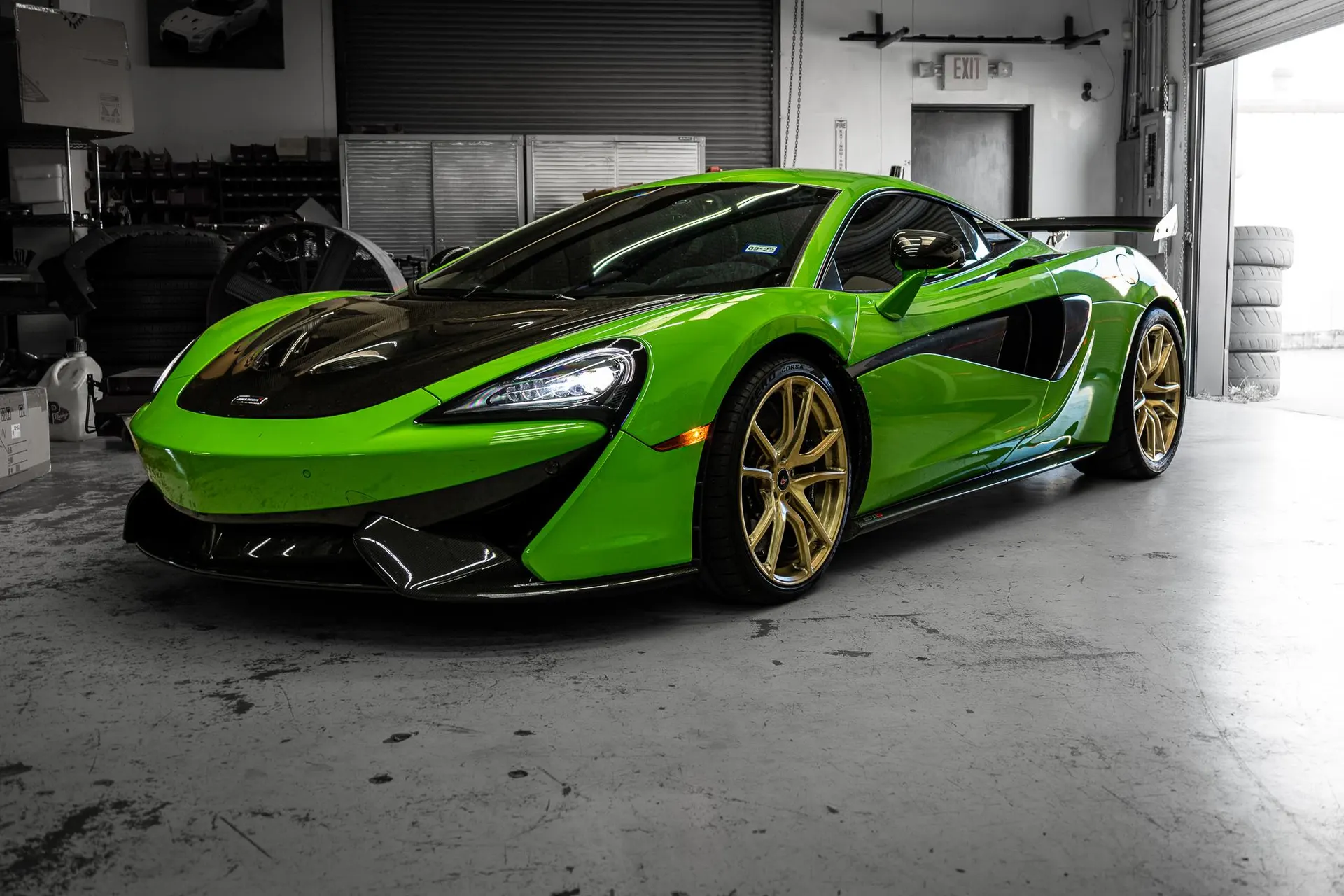Bright green McLaren 570S with black accents and gold wheels parked inside a performance tuning shop.