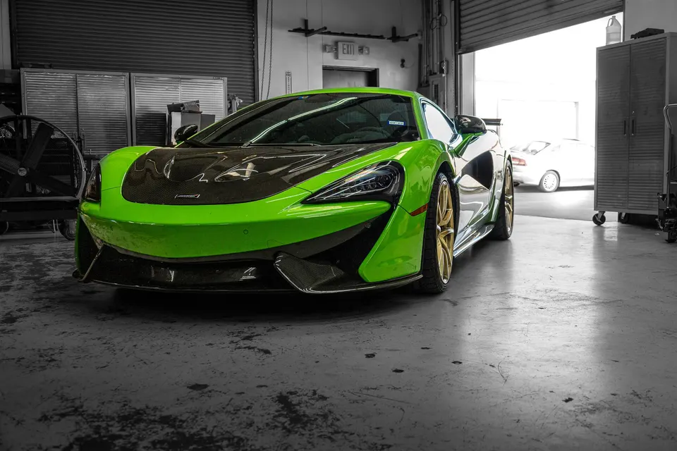 A vibrant green McLaren supercar with a carbon fiber hood and gold wheels parked inside a clean performance tuning shop.