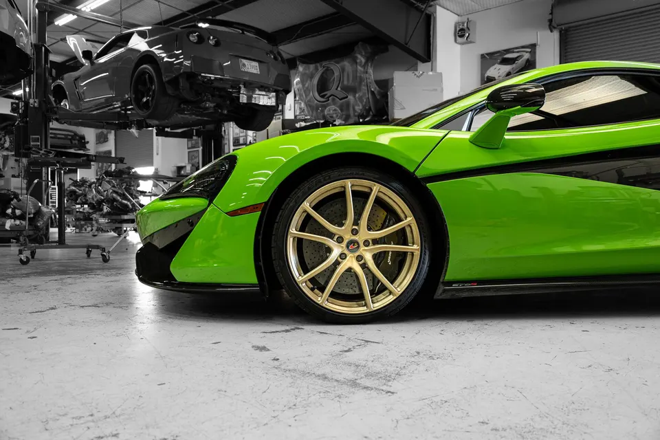Green McLaren with gold wheels in a performance tuning shop, with a Nissan GT-R on a lift in the background.