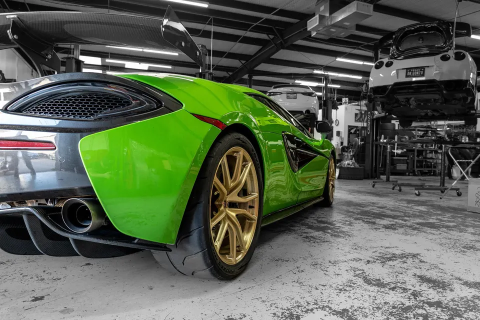 A vibrant green McLaren with a large carbon fiber wing and gold wheels parked in a performance tuning shop.
