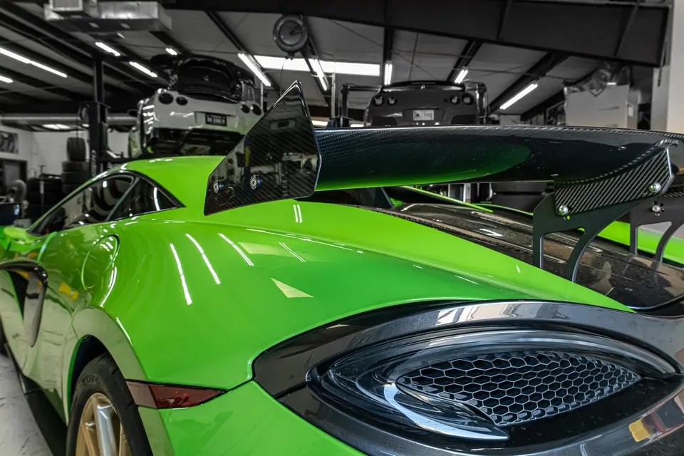 A bright green McLaren supercar with a large carbon fiber rear wing parked inside a performance tuning shop.