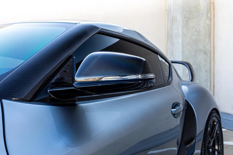 Close-up detail of a grey Toyota Supra with carbon fiber A-pillar trim and side mirror housing