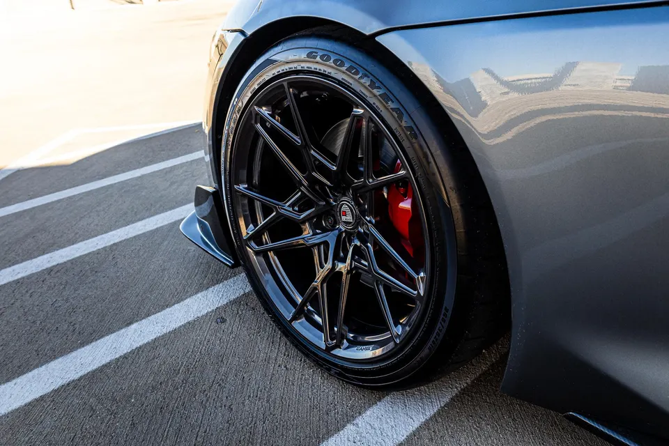 A close-up detail shot of a grey car's black multi-spoke wheel, Goodyear tire, and red brake caliper.