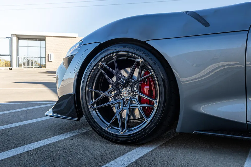 Close-up of a grey sports car's front wheel, featuring custom multi-spoke wheels, red brake calipers, and Goodyear tires.