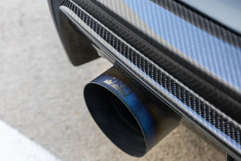 A close-up of a blue-tinted HKS titanium exhaust tip and carbon fiber rear diffuser on a performance car.