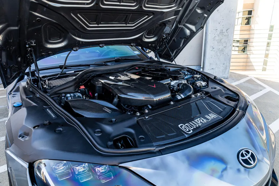 A close-up view of a custom carbon fiber engine bay in a Toyota Supra.