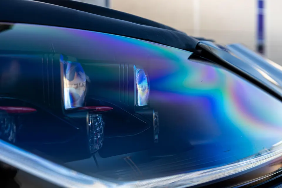 Close-up detail of a car's headlight with iridescent reflections on the lens, showcasing intricate design.